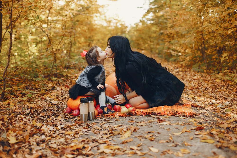 A mother and daughter sharing a kiss with some pumpkins